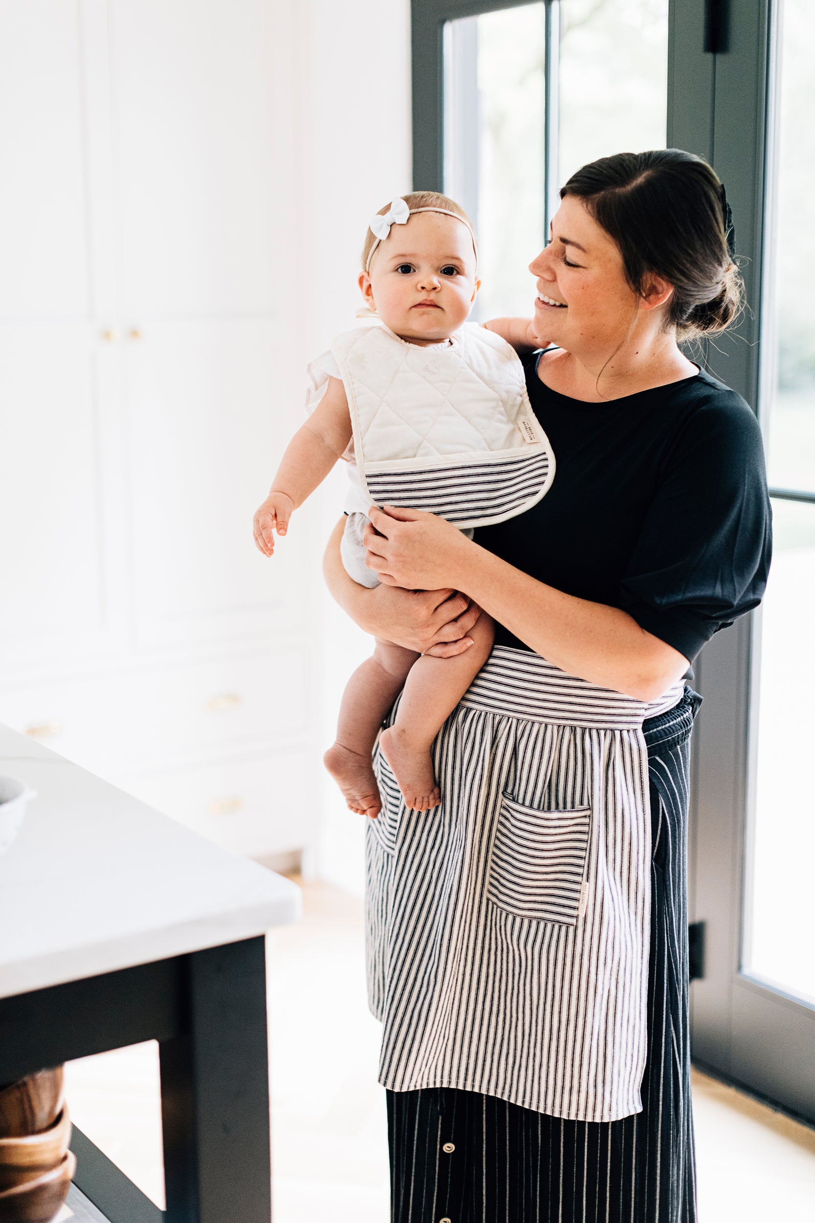 The Adult Ticking Apron on a Model Holding a Baby